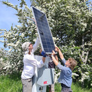 Photo of three people attaching a solar panel to the top of a pole holding a CRNS device | photo: Cosmic Sense Consortium