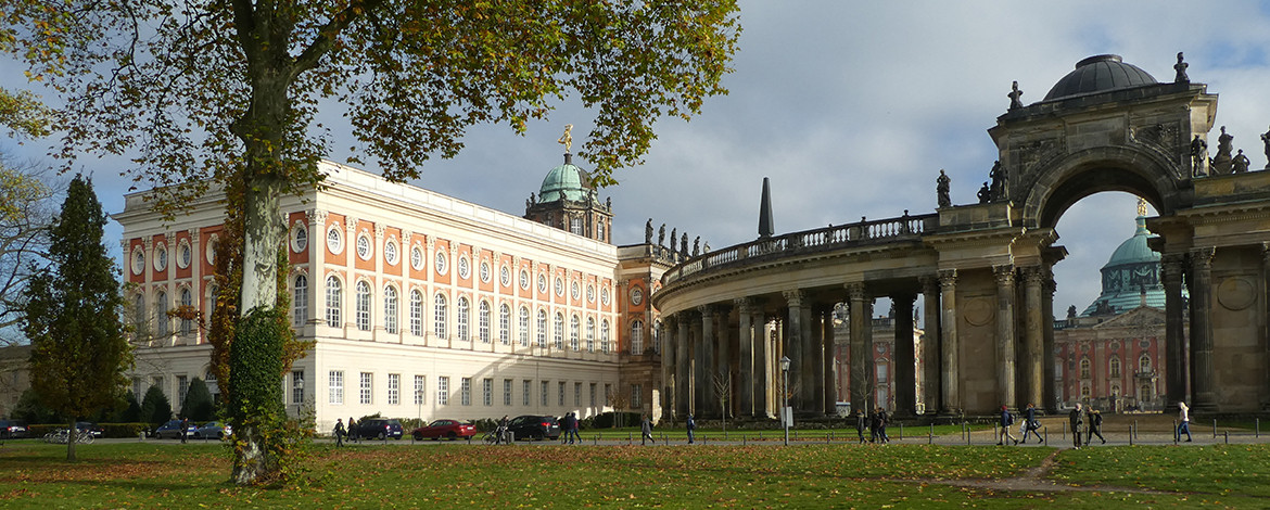 Haus 11 am Neuen Palais im Herbst. Das Haus besteht aus rosa-rotem Backsteinmauern mit weißem Stuck, der Fenster, Türen und Dach verziert. Rechts daneben Säulengang mit Rundbogen.