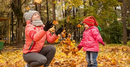 Eine Frau und ein Kind spielen im Herbstlaub. Die Frau wirft das Laub nach oben.