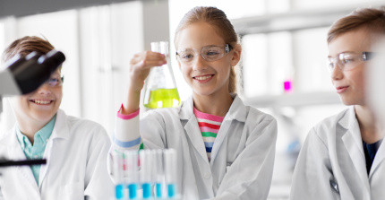 Drei Schüler*innen stehen am Labortisch und schauen auf einen Kolben mit gelber Flüssigkeit.