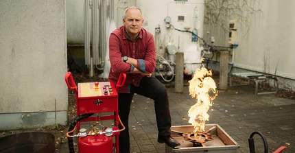 Ulf Lepszy posiert neben Flamme und Feuerlöscher.