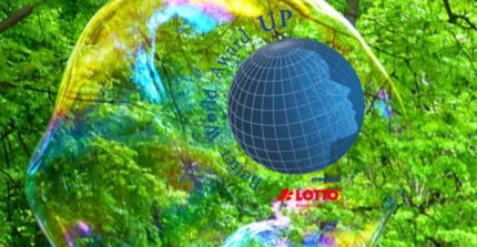 Ein Globus umgeben mit Schrift "Better World Award" und "powered by Lotto Brandenburg". Im Bildhintergrund das grüne Laubdach eines Waldes und große Seifenblasen.