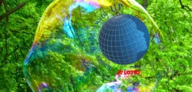 Ein Globus umgeben mit Schrift "Better World Award" und "powered by Lotto Brandenburg". Im Bildhintergrund das grüne Laubdach eines Waldes und große Seifenblasen.