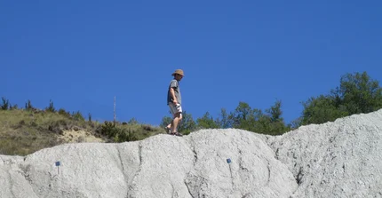 Ein Mann in kurzer Hose und mit Hut geht auf einem Gebirgsrand entlang