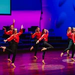Sechs Tänzerinnen der Animá Ladies in schwarz-roten Kostümen tanzen eine Choreo aus ihrem Bachata Tanzkurs auf der Bühne.