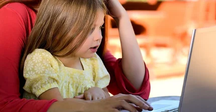 Eine Frau hat ein Kind auf dem Schoß, beide schauen auf einen Laptop.