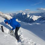 Field site Zugspitze: Scientist digging a snow pit at a steep hillslope with white mountains in the background | Photo: Cosmic Sense Consortium