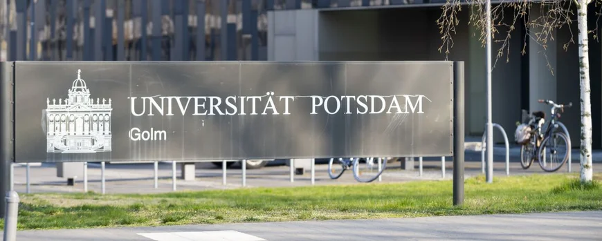 Sign with lettering "University of Potsdam" in front of the facade of a black building