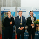 Vier Personen, eine hält eine Statuette und einen Blumenstrauß