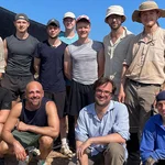 Gruppenbild der Angehörigen der Universität Potsdam am Grabungsort. Es sind elf Personen auf dem Bild zu erkennen. Sie alle tragen Kleidung, die praktisch und funktional ist beim körperlichen Arbeiten in Sand und Sonne.