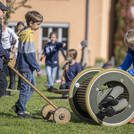 Kinder spielen an Pedalo-Spielgeräten und rollen in einer Holztonne.