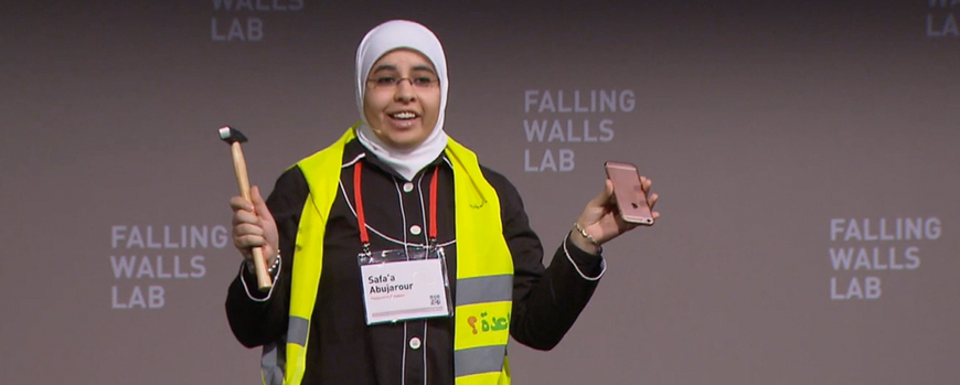 Safa'a holding up hammer and smartphone on the stage