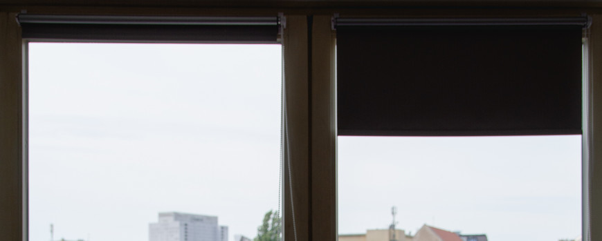 Ein Student sitzt an seinem Schreibtisch vor einem großen Fenster. Draußen sieht man Bäume und große Hochhäuse. Vor sich hat er ein Buch und seinen Computer