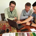 Drei Männer sitzen an einem Tisch und schauen in einen Laptop