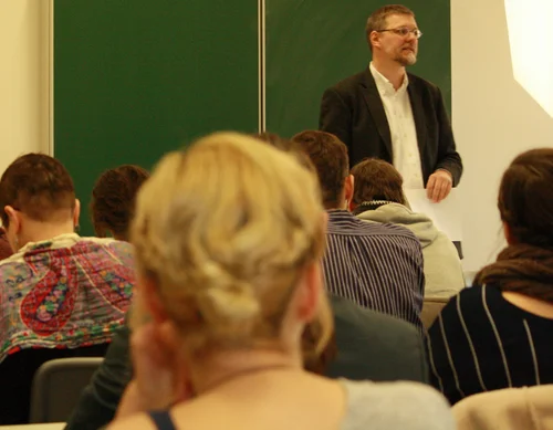 Eine Seminarsituation im Rahmen der Ringvorlesung "Was sind Jüdische Studien?" im Winter 2014. Hinterköpfe von Studierenden im Vordergrund. Prof. Dr. Thomas Brechenmacher im Hintergrund vor einer Tafel.