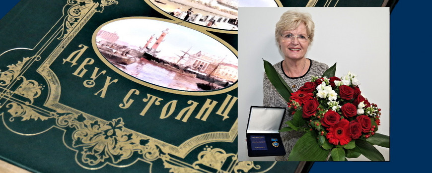 Dr. Doris Gebert mit Medaille und Blumen, vor dem Hintergrund des Buchgeschenks