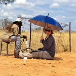 Two NamTip researchers collecting data from a soil probe, one of them holding an umbrella to protect herself from the sun