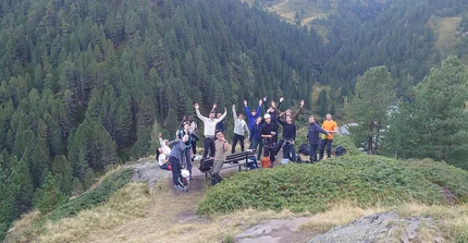 Gruppenfoto vor alpiner Bergkulisse. Die Menschen winken und geben Peace-Zeichen.