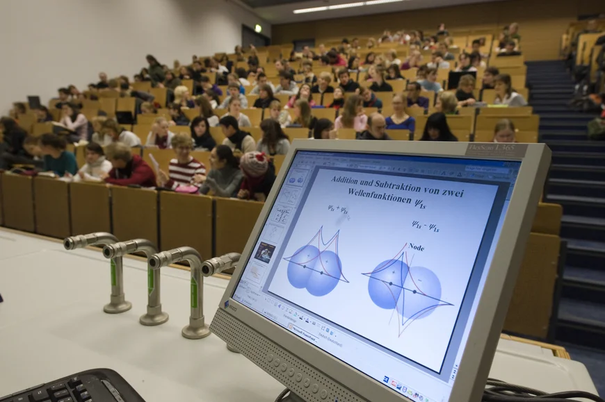 Hörsaal mit Studierenden im Vordergrund eein Bildschirm mit Mathematischer Zeichnung