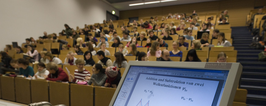 Hörsaal mit Studierenden im Vordergrund eein Bildschirm mit Mathematischer Zeichnung