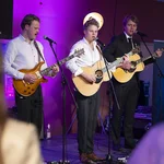 Drei Musiker mit Gitarre auf einer Bühne.