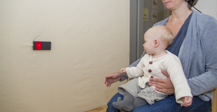 A child sits on their mothers lap and looks at a red light at the side of the room