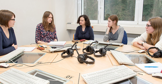 5 Personen sitzen zusammen um einen Schreibtisch.