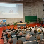 Ein Hörsaal mit Personen im Saal und einer Person auf dem Podium