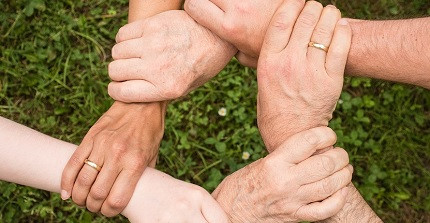 Sechs Hände von Menschen unterschiedlichen Alters halten einander fest.