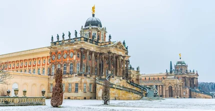 zwei historische Gebäude am Neuen Palais hinter verschneiten Wiesen