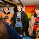 Drei Personen mit bunten T-Shirts an einem Marktstand
