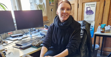 Maraike Hofer at her desk in front of two monitors sits next to mineral samples
