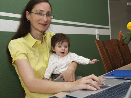 Eine Professorin arbeitet am Computer mit einem kleinen Kind auf ihrem Schoß. Foto: Karla Fritze