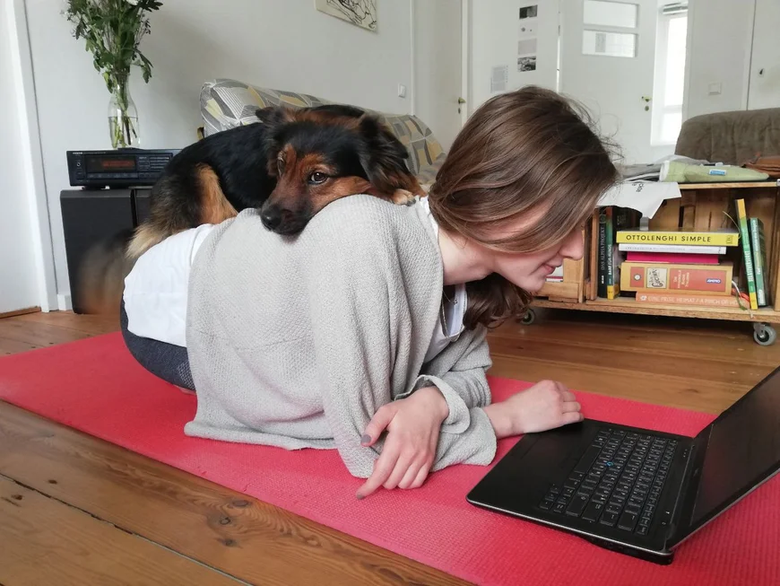 Eine junge Frau hockt halbliegend auf dem boden über einem Buch. auf ihrem Rücken sitzt ein Hund