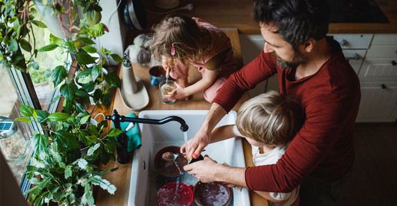 Mann mit zwei Kindern steht in der Küche und wäscht ab. Das Foto ist von AdobeStock/Halfpoint.