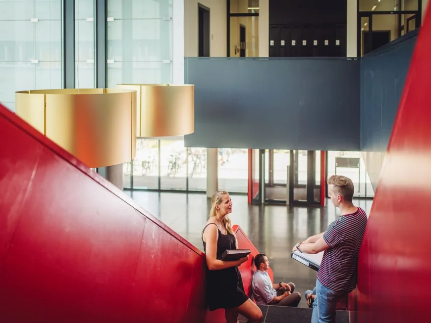 Eine Studentin und ein Student stehen in Haus 28 in Golm auf einer Treppe und unterhalten sich.