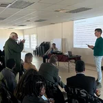 Rund 20 Menschen sitzen in einem Raum, einer steht vorn, sie diskutieren miteinander