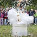 Wasserfontäne aus einer weißen Tonne, im Hintergrund Zuschauer