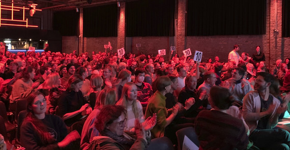 sitzendes Publikum in einer Halle, mit roten Licht angestrahlt