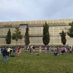Kinder auf einer Wiese mit Spielgeräten vor einem goldfarbenen Institutsgebäude.