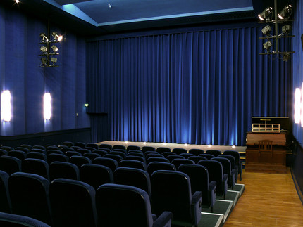 Kinosaal mit dunkelblauen Sitzen, einem dunkelblauen Vorhang und in der Ecke eine Kinoorgel