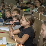 Kind mit Mikrofon in einem Hörsaal voller Kinder