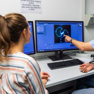 This image shows a scientist and a doctoral students speaking in front of a monitor.