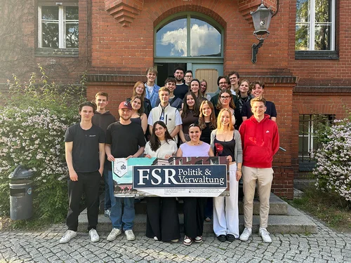 Mehrere Personen stehen vor einem Backsteingebäude, im Vordergrund halten sie ein Banner mit der Aufschrift "FSR Politik und Verwaltung"