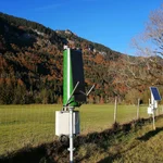 Field site Graswang: Two CRNS sensors with solar panels installed next to a single tree at a green pasture valley bottom. In the background are mountains with mixed autumn forest | Photo: Cosmic Sense Consortium