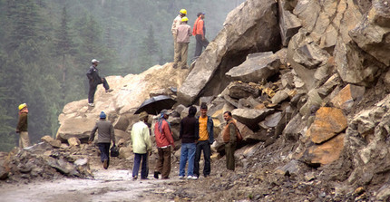 Menschen an von Steinen verschütteter Straße nach Lawine im Gebirge