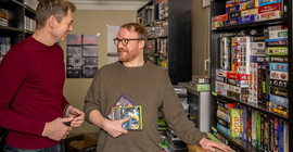 Prof. Dr. Jan Distelmeyer (l.) und Prof. Dr. Sebastian Möring (r.) stehen in einem Raum voller Spiele.