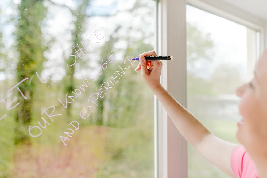 Frau schreibt einen Schriftzug am Fenster