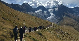 Menschen wandern einen Pfad entlang, im Hintergrund hohe Berge