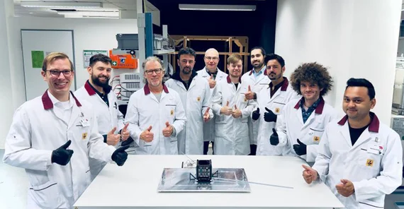 TU Berlin engineering team with CyBEEsat in a lab. Everyone is wearing white lab coats.